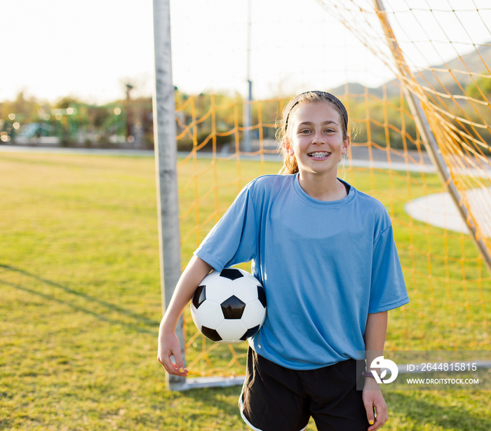 Portrait of cheerful girl holding soccer ball while standing against net