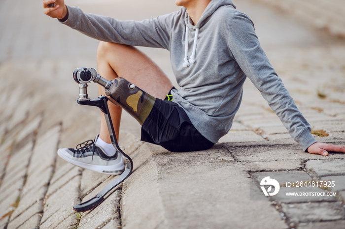 Cut out picture of handsome caucasian handicapped sportsman in sportswear and artificial leg sitting