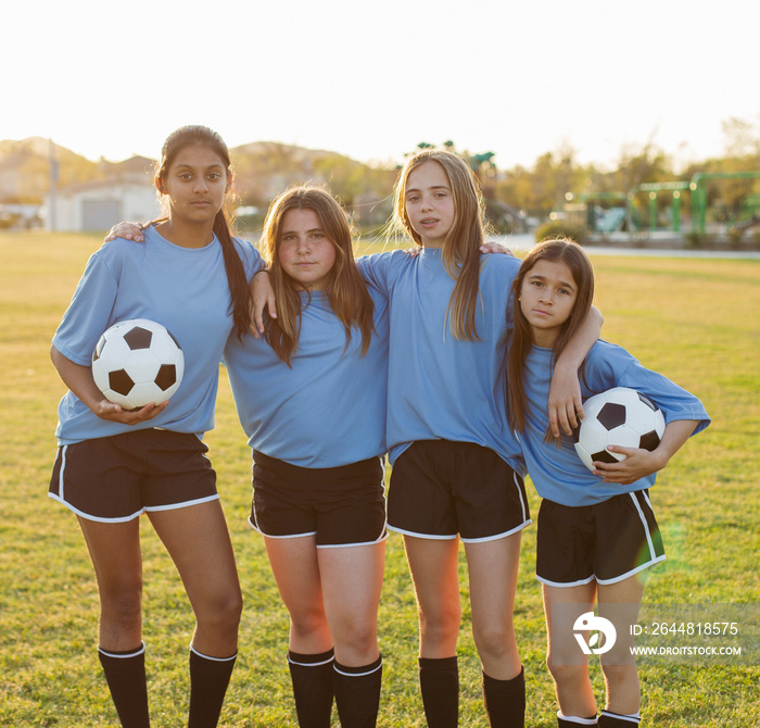 Portrait of confident girls with arms around standing on soccer field against clear sky