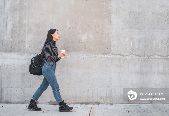 Asian woman walking and holding a cup of coffee.