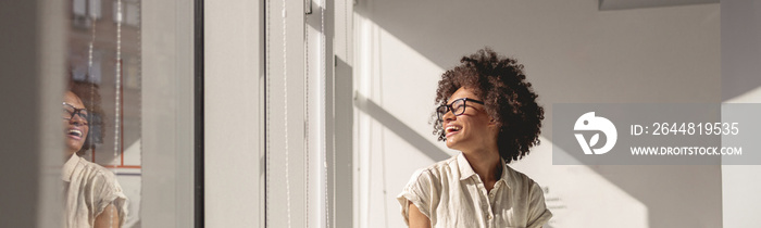 Happy woman in glasses sitting on the table while holding notebook and looking out the window