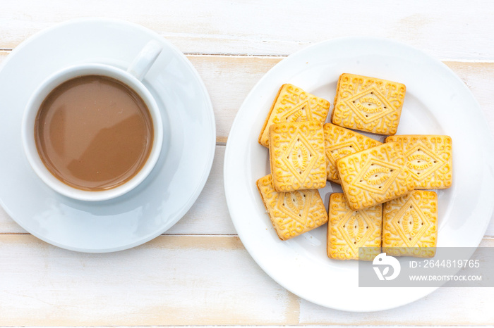 Several custard cream biscuits on a white plate with a cup of coffee in the background on a white ta