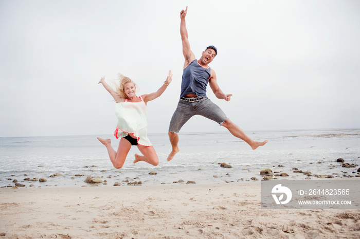 Pregnant couple jumping mid air on the beach