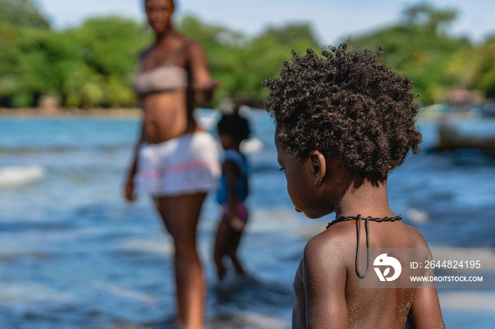 Imagen horizontal de un pequeño niño afroamericano con cabello afro de espalda en la playa en un día