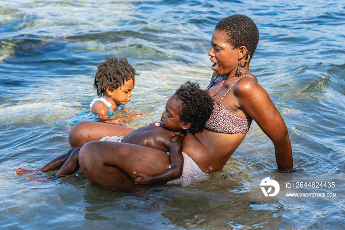 Imagen horizontal de una madre y sus pequeños hijos afroamericanos jugando juntos a la orilla del ma