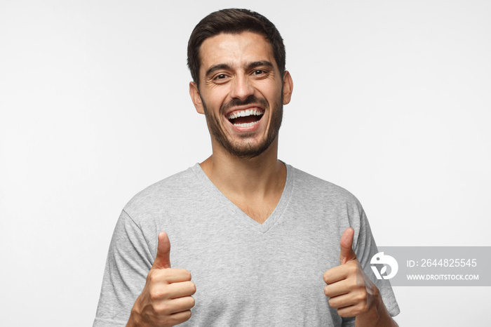 Laughing young man in gray t-shirt making a thumbs up gesture of approval and success