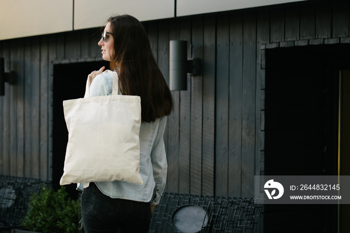 Woman holding white textile eco bag against urban city background. . Ecology or environment protecti