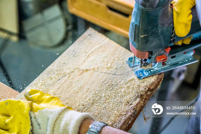 Carpentry background. Carpenter hands with fretsaw. Carpenter use electric fretsaw to cut the desk. 