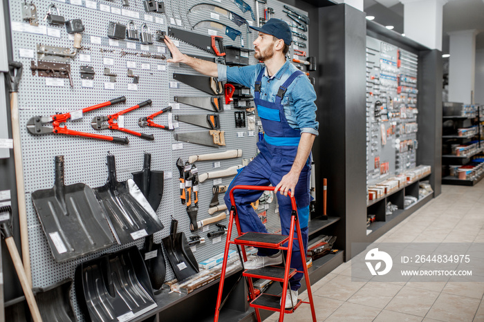 Portrait of a handsome worker in uniform standing on the ladder near the showcase with garden equipm