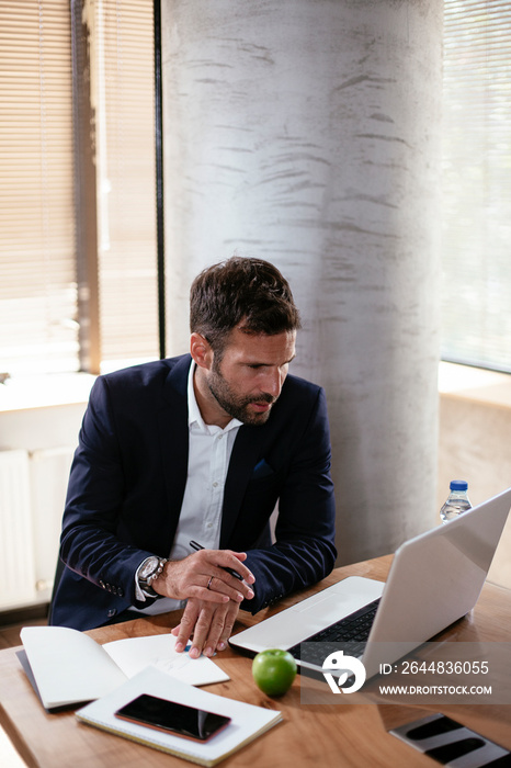 Young businessman using laptop in his office. Businessman taking a notes while working on laptop