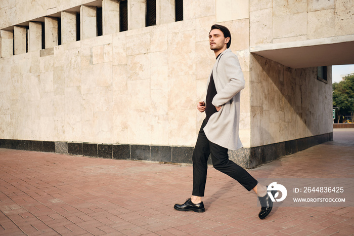 Young handsome stylish man in coat confidently walking outdoor