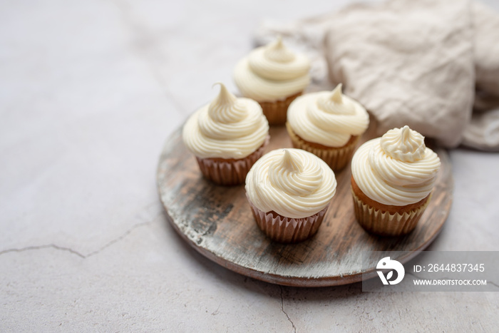 Mini muffins in paper cupcake holder on the wooden tray with white cream cheese frosting