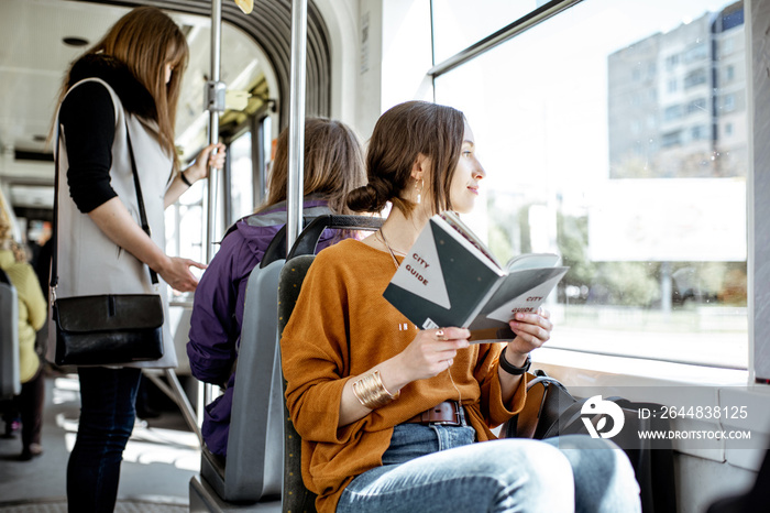 Young woman reading book while moving in the modern tram, happy passenger at the public transport