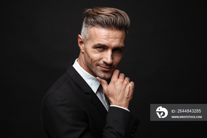 Handsome mature business man posing isolated over black wall background.