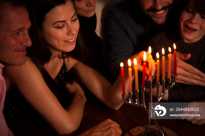 Multigenerational family looking at smiling woman burning candles on menorah during Hanukkah at home