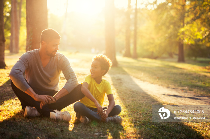 Happy family siting on grass in the park enjoying sunset.