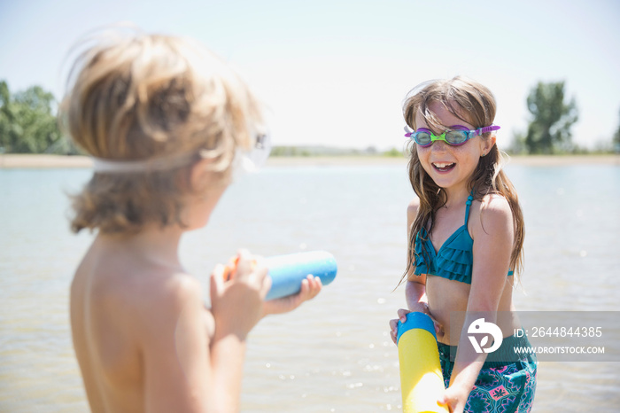 Siblings playing with water guns in the lake