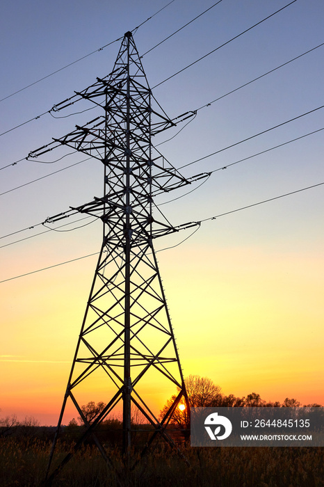 Silhouette of pylon and high voltage power lines against a colorful sky at sunrise or sunset