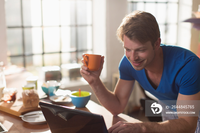 Man drinking coffee at laptop in morning kitchen