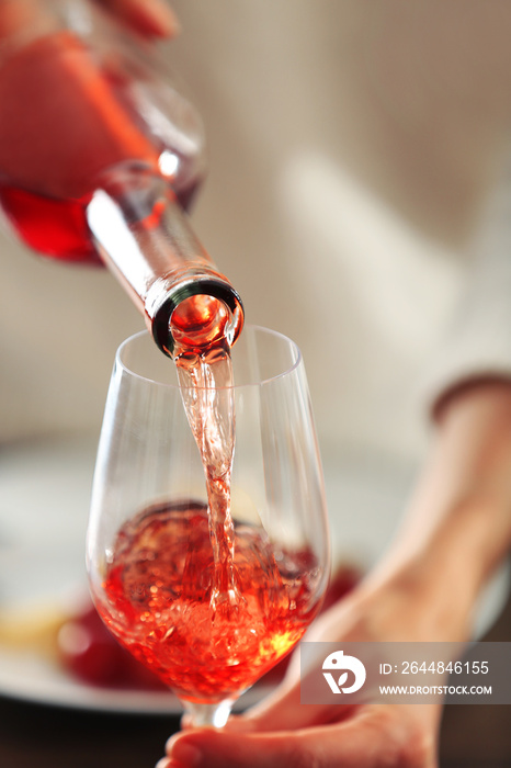 年轻女子将粉红色的葡萄酒倒入桌子上的玻璃杯