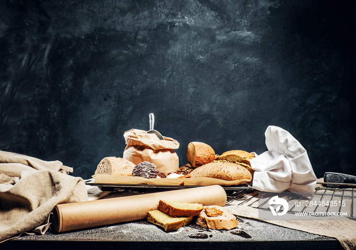 Freshly bread baguettes and muffins on a wooden table in a dark studio