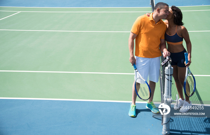 Woman kissing cheek of man beside tennis court net