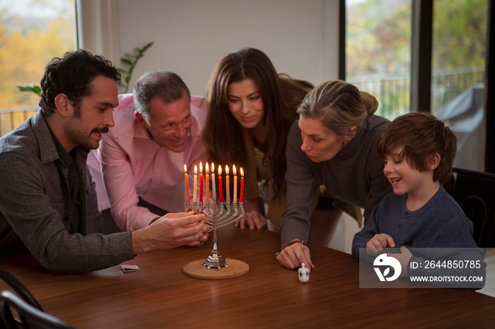 Happy multigenerational family playing dreidel on table during Hanukkah festival