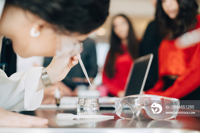 Female student adding solution in container during chemistry class at university