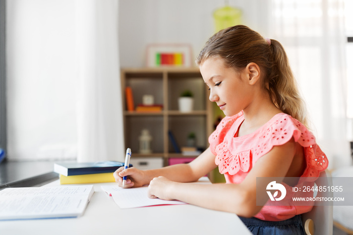 children, education and learning concept - student girl with book writing to notebook at home