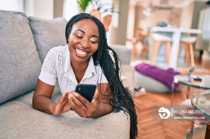 Young african american woman smiling happy using smartphone laying on the sofa at home