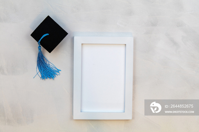 White frame mockup with Graduation cap and royal blue tassle on gray wash background flat lay copy s