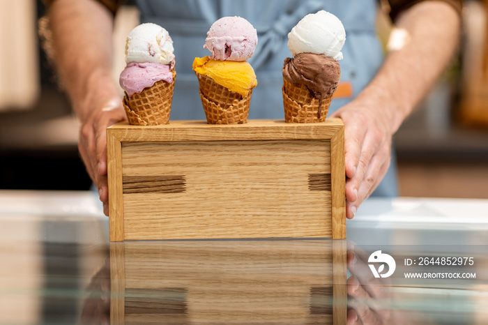 Seller putting a stand with three yummy ice creams in waffle cones with different flavor on the coun