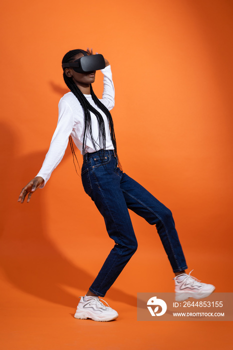Falling African-American girl with vr glasses holding her arms out to her sides on orange background