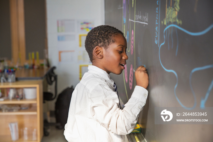 Side view of student writing on blackboard in classroom