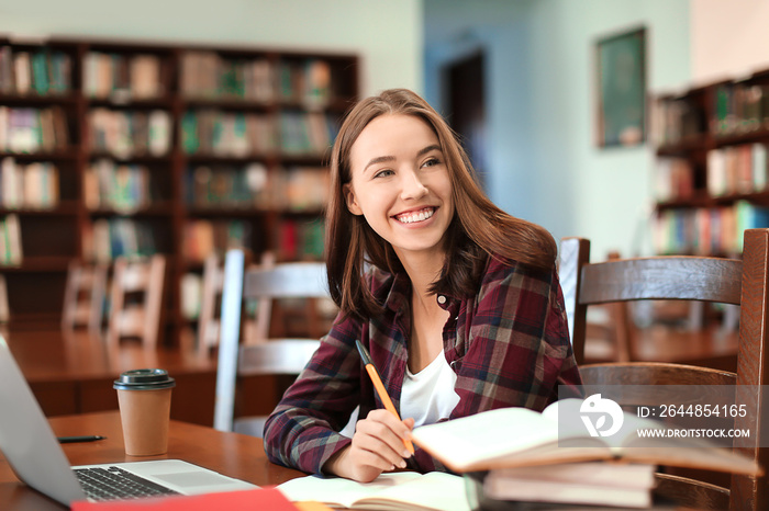 漂亮的学生拿着笔记本电脑在图书馆学习