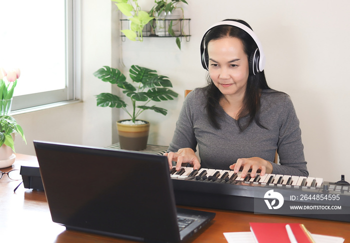 Asian woman learning music lesson online , playing electric piano with  computer notebook.  Teaching