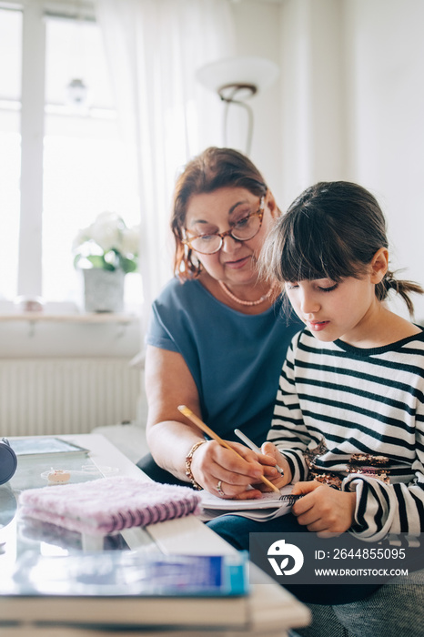 Grandmother assisting girl in homework on sofa at home