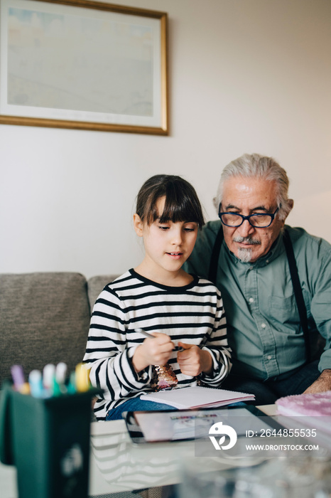 Senior man assisting female kid in homework at living room