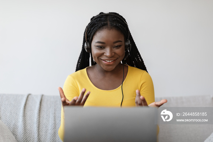 Teleconference. Cheerful young black woman in headset having video call on laptop