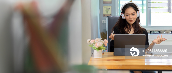 Female online studying with digital tablet and wearing headphone while sitting at table in living ro