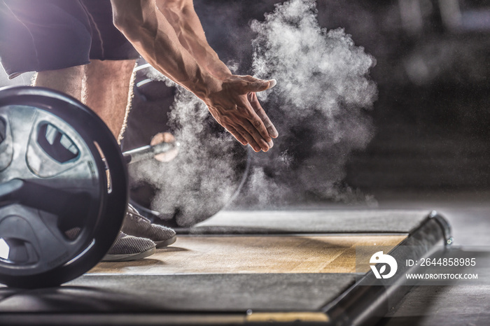 Muscular weightlifter clapping hands before barbell workout at the gym with dumbbells