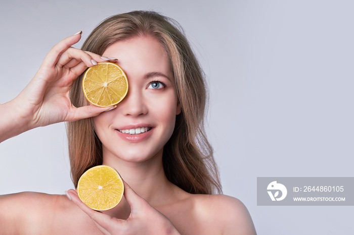 portrait of pretty young woman holding slices of orange, facial care