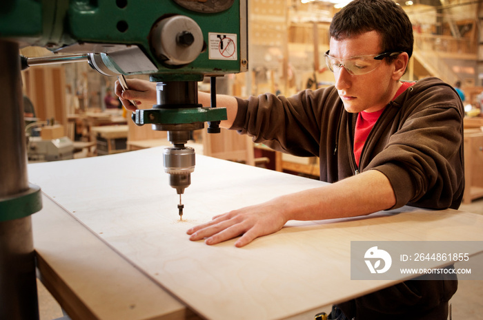 Carpenter drilling wooden plank at workshop