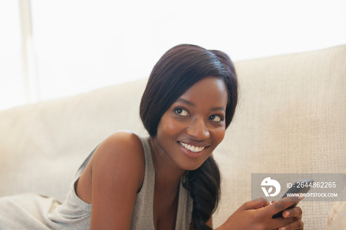 Smiling young woman using smart phone on sofa