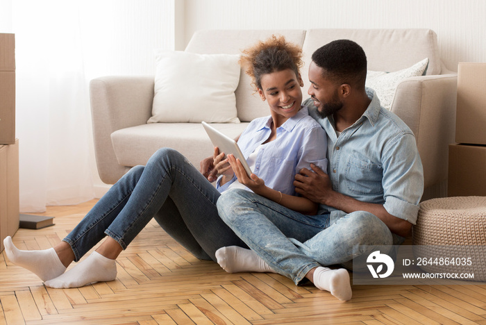 Couple Using Tablet Sitting Among Moving Boxes In New Apartment