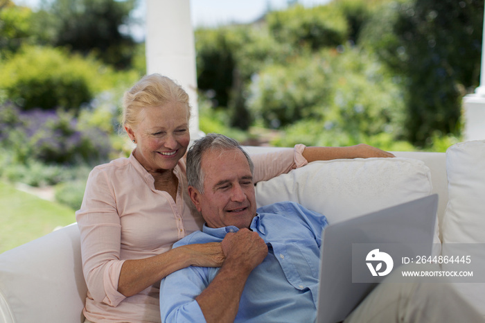 Senior couple using laptop on patio sofa