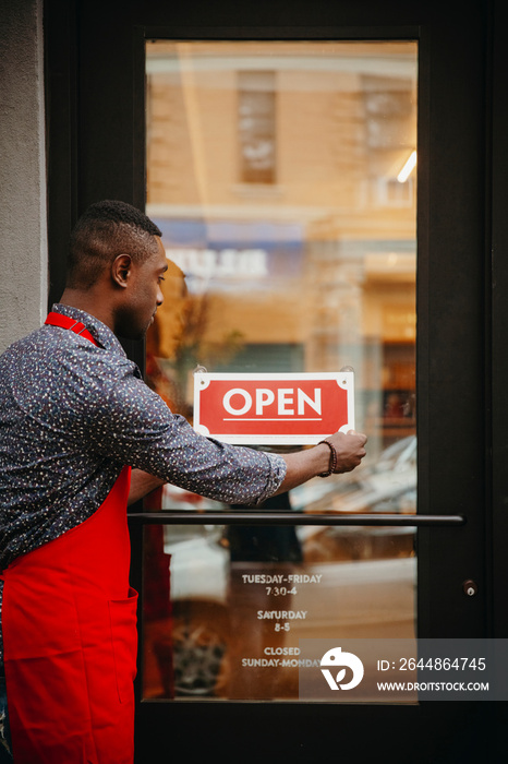 Side view of male owner putting open sign on door at cafe