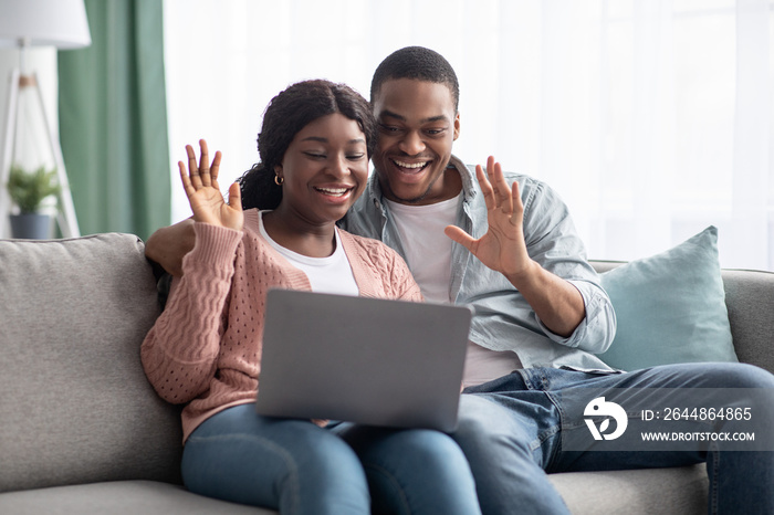 欢快的黑人夫妇在笔记本电脑屏幕前挥手，家里