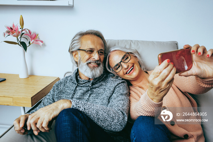 Happy senior couple at home smiling  on couch and looking at mobile phone together