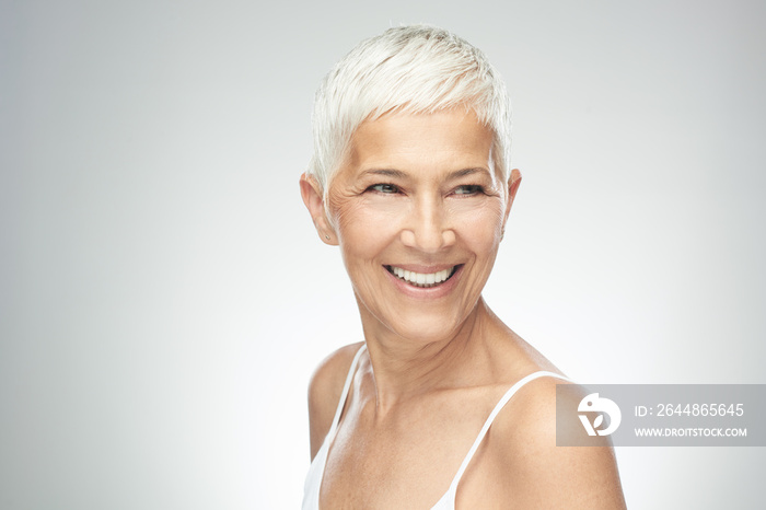 Beautiful smiling senior woman with short gray hair posing in front of gray background. Beauty photo